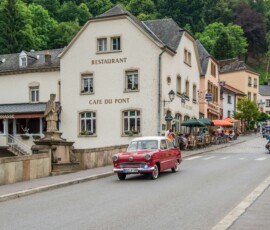 Illustratie: foto vanaf de straat in Vianden waaraan Café Du Pont ligt. Op de foto rijdt een rode oldtimer over de brug. Fotograaf: Marcel de Hoog.