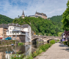 Van de overzijde van het water gemaakte foto. Rechts op de foto is de brug te zien waaraan het café haar naam dankt, links is ons gezellige horeca-etablissement te zien en in de verte op de berg prijkt het kasteel van Vianden.